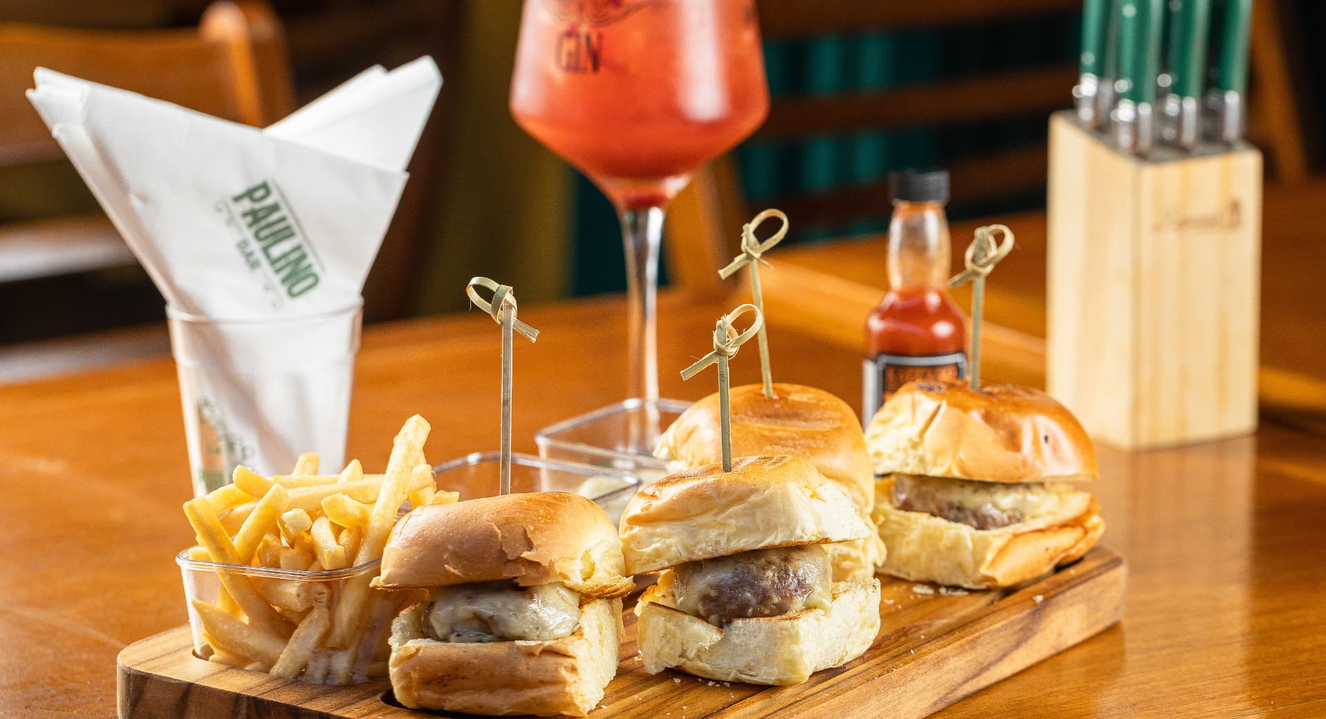 Porção de hambúrguinhos artesanais com fritas e drink na tábua do Paulino Bar